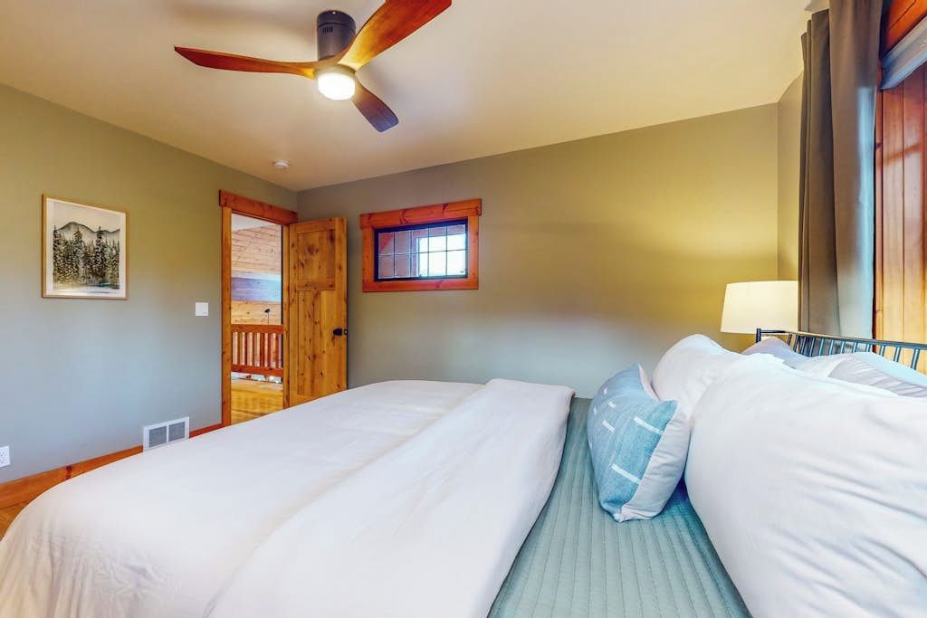A bedroom with two beds, a ceiling fan, a window, and a door.