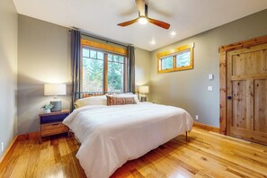 Ein Schlafzimmer mit einem Bett, Holzboden, Deckenventilator, einem Fenster mit Vorhängen und einer Holztür.