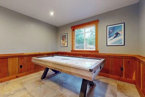Ein Zimmer mit Holzboden, einem zentral platzierten Eisstocktisch, Holzvertäfelung an den Wänden und einem Fenster mit Blick auf Bäume.