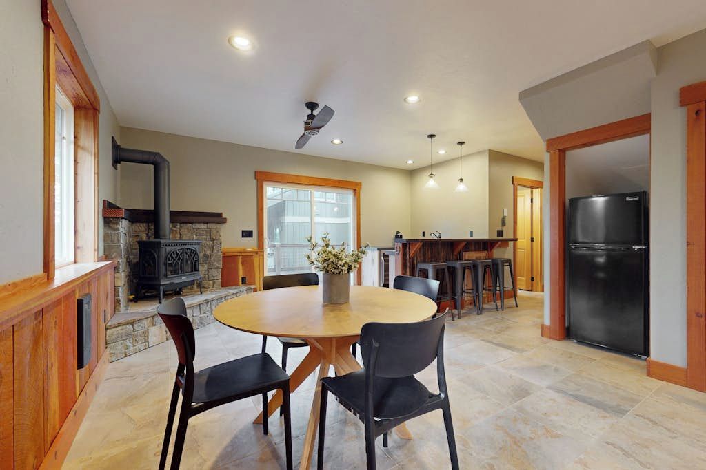 A spacious kitchen with a stone fireplace, a round dining table with chairs, and a refrigerator.