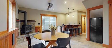 A spacious kitchen with a stone fireplace, a round dining table with chairs, and a refrigerator.