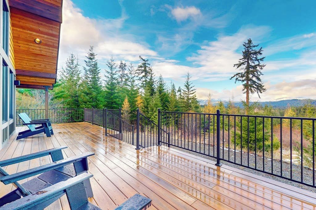 A wooden deck with a metal railing, overlooking a forested area with evergreen trees.