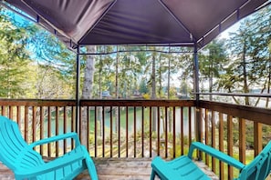 A covered outdoor deck with two turquoise chairs, a wooden railing, and a view of a lake and trees.