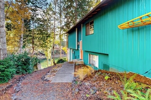 A house with a green exterior, a concrete pathway leading to the entrance, and a pond in the background.