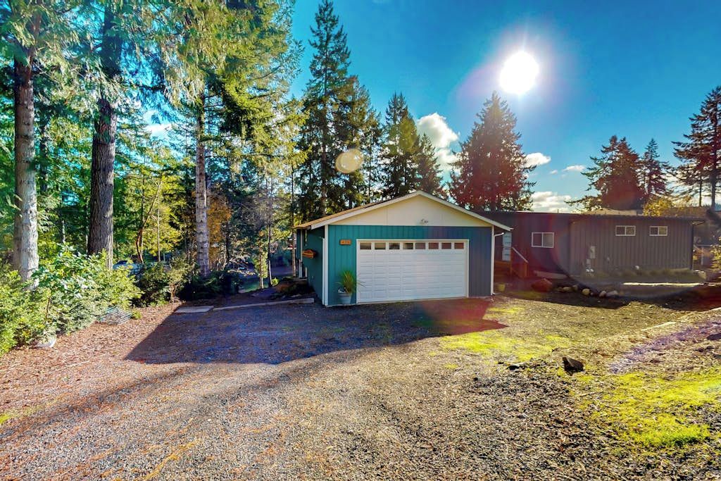 A single-story building with a garage, surrounded by trees and a gravel driveway.