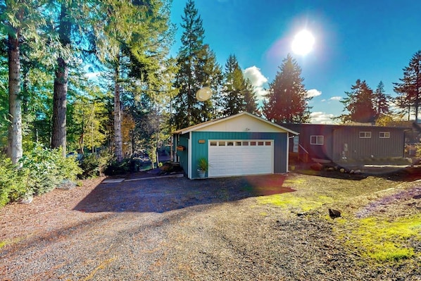 A single-story building with a garage, surrounded by trees and a gravel driveway.