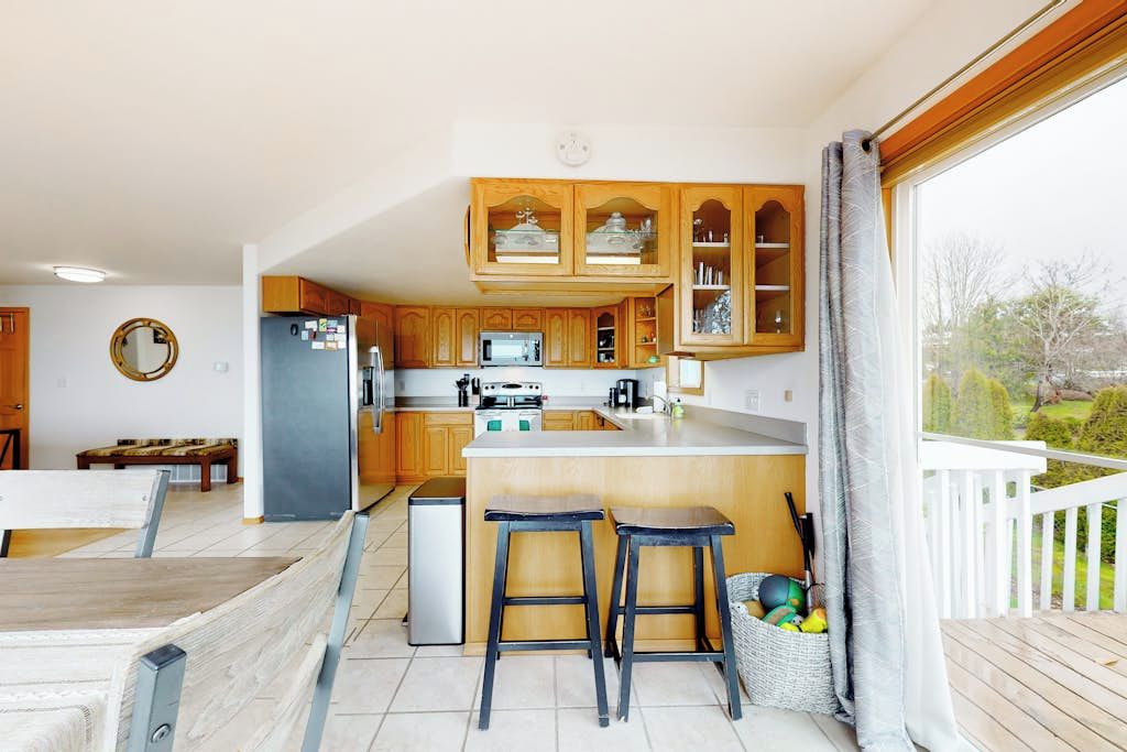 Una cocina moderna con armarios de madera, un microondas integrado y un refrigerador pequeño. Hay dos taburetes en la isla de la cocina y una cesta con pelotas deportivas.