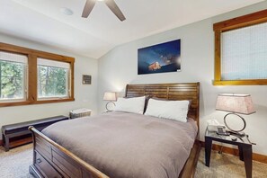 Een slaapkamer met een bed, nachtkastje, lamp, raam en plafondventilator.