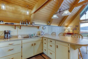 A kitchen with wooden cabinets, a sink, and a dining area with chairs. - 1BR A-frame oceanfront (Anacortes)