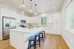 A modern kitchen with white cabinetry, a central island with bar stools, stainless steel appliances, and pendant lighting.