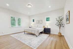 A bedroom with a bed, bedside tables, a rug, a window with blinds, and a potted plant. - 2BR lakefront home with private dock and fireplace (Stanwood)