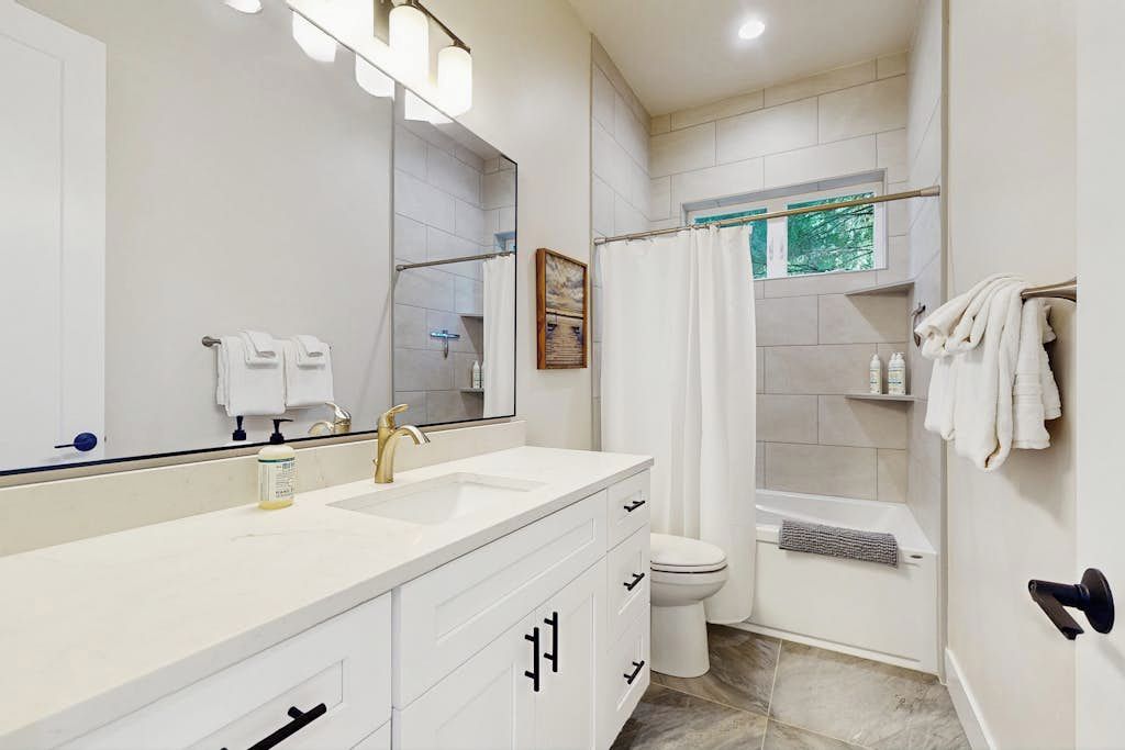A modern bathroom with a large mirror, dual sinks, a toilet, and a shower area.