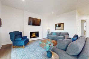 A modern living room with a fireplace, a sofa set, a blue armchair, and a coffee table with a vase. - 2BR lakefront home with private dock and fireplace (Stanwood)