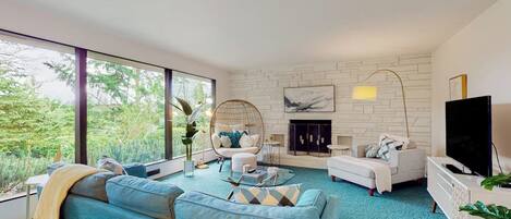 A modern living room with a sofa, armchair, and coffee table, a fireplace, and a television.