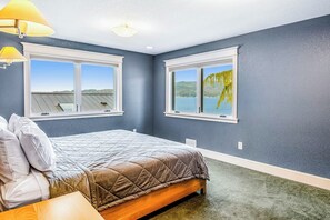 A bedroom with a bed, two windows, a lamp, and a view of a body of water. - Lovely 3BR Lakefront - Dock - Fireplace (Bellingham)