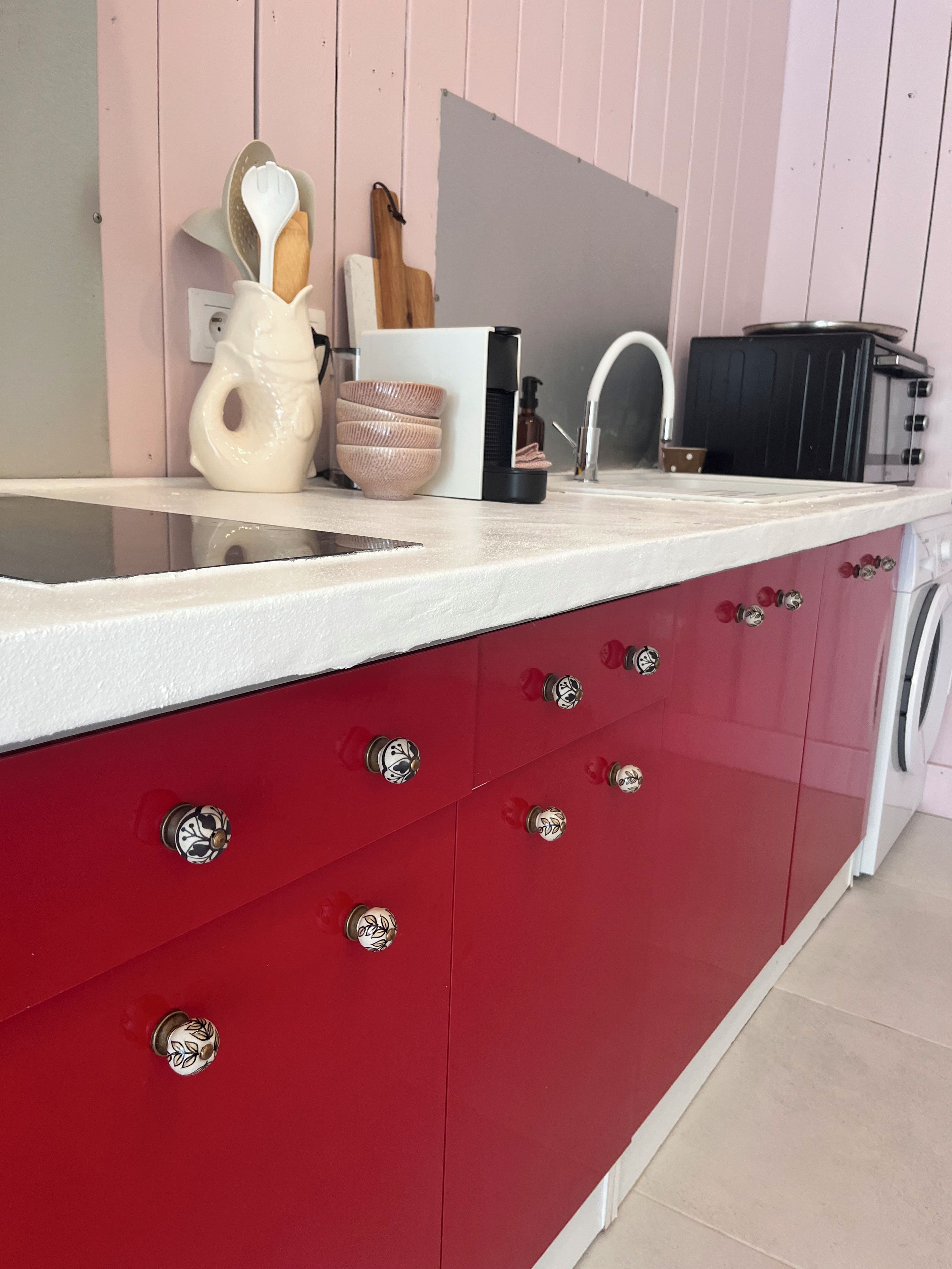 Una cucina con piano di lavoro bianco, pensili rossi e lavello in acciaio inossidabile.