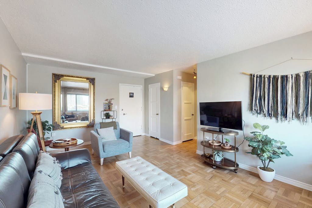Ein Wohnzimmer mit Sofa, Sesseln, Hocker, Fernseher und einer Pflanze.