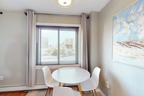 Ein Zimmer mit einem runden Tisch, vier Stühlen, einem großen Fenster mit Jalousien und einem Gemälde an der Wand.