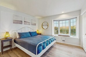 Ein Schlafzimmer mit einem Bett, Nachttischen, einem Fenster mit Blick und Wandbildern.