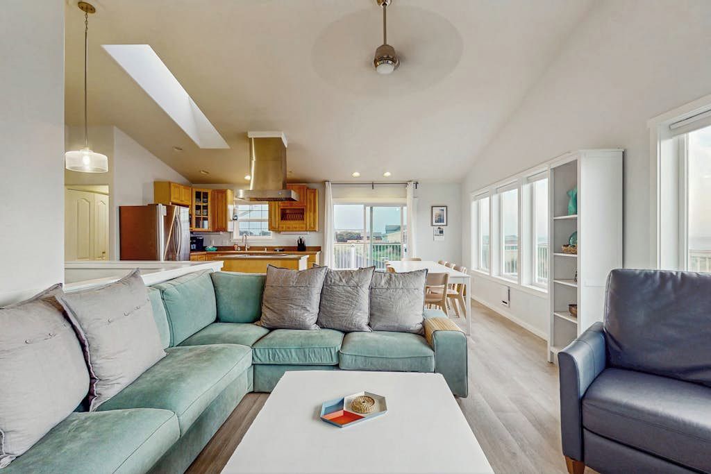 A modern living room with a sofa, a coffee table, and a dining area in the background.
