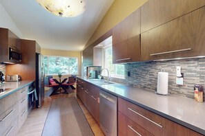 A modern kitchen with dark wood cabinets, a stainless steel microwave, and a large window providing natural light. - Forest 3BR in Shoreline with patio & yard (Shoreline)