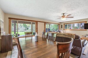 A spacious dining area with a wooden table and chairs, a ceiling fan, and large windows offering a view of the outdoors. - Large 3BR Riverfront Dog Friendly - Hot Tub (Easton)