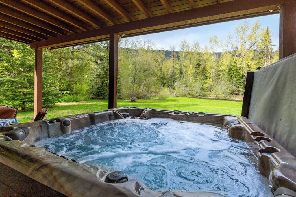 Ein Whirlpool mit einer hölzernen Pergola darüber, umgeben von üppiger, grüner Landschaft.