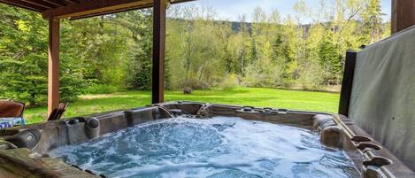 A hot tub with a wooden pergola overhead, surrounded by a lush green landscape.