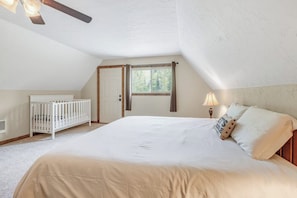 A bedroom with a large bed, a crib, a window, and a ceiling fan. - Large 3BR Riverfront Dog Friendly - Hot Tub (Easton)