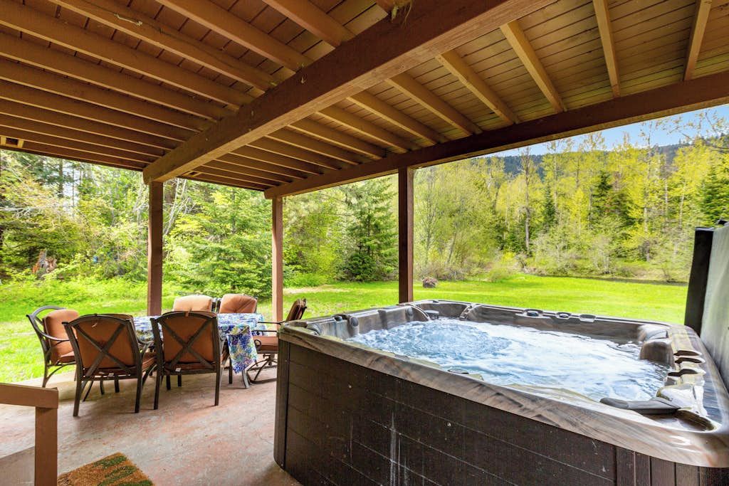Een hottub onder een houten pergola met een tafel en stoelen, omgeven door een weelderig groen landschap.