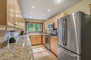 A kitchen with granite countertops, stainless steel appliances, wooden cabinets, and a window with a view of trees. - Large 3BR Riverfront Dog Friendly - Hot Tub (Easton)