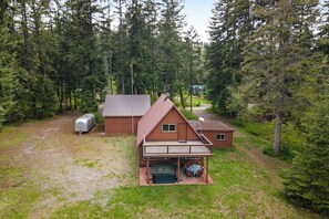 A cabin with a porch, a covered outdoor seating area, and a trailer in a forested area. - Large 3BR Riverfront Dog Friendly - Hot Tub (Easton)