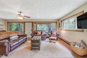 A spacious living room with leather sofas, a vintage trunk, and a ceiling fan. - Large 3BR Riverfront Dog Friendly - Hot Tub (Easton)
