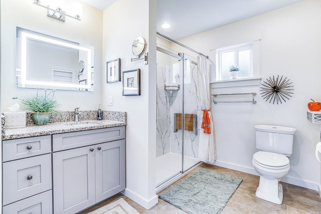 Un baño con cabina de ducha de vidrio, inodoro blanco y encimera de granito con lavamanos.