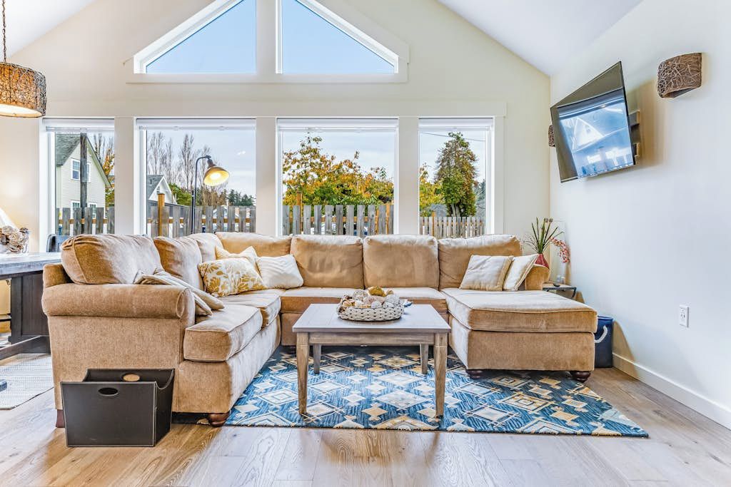 A spacious living room with a large sectional sofa, a coffee table, and a TV mounted on the wall.