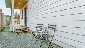En terrasse med et træbord og to stole, en træterrasse og en hvid bygning med facadebeklædning.