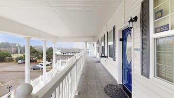 A covered porch with a white railing, a blue door, and a view of a parking lot.