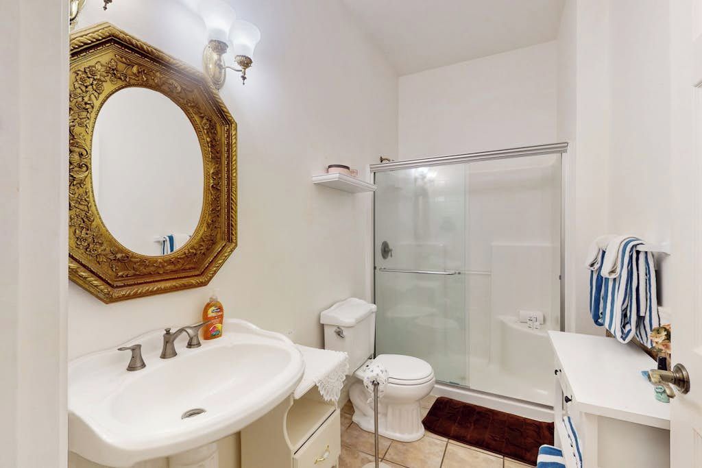 Un baño con un lavamanos blanco, un inodoro, una cabina de ducha y un espejo grande y decorativo.