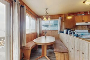 Ein Holzinnenraum mit rundem Tisch und Bänken, einer Küchenzeile mit Schränken und Blick durch ein Fenster.