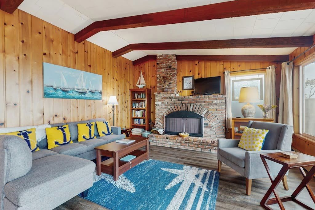 A cozy living room with a fireplace, wooden walls, a sofa, a coffee table, and a bookshelf.