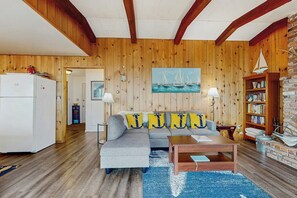 A cozy living room with a wooden wall, a grey sofa, a coffee table, and a bookshelf. - 2BR Birch Bay: 3 Steps to Beach (Blaine)