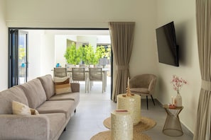 A modern living room with a sofa, a TV mounted on the wall, and a dining area with chairs and a table. - "Altura" | Luxury 3BR Penthouse by Mambo Beach (Willemstad)