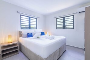 Une chambre d’hôtel comprenant un lit, deux fenêtres équipées de stores, une table de chevet avec une lampe et une armoire.