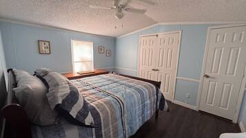 A bedroom with a bed, a ceiling fan, a window with blinds, and a door.