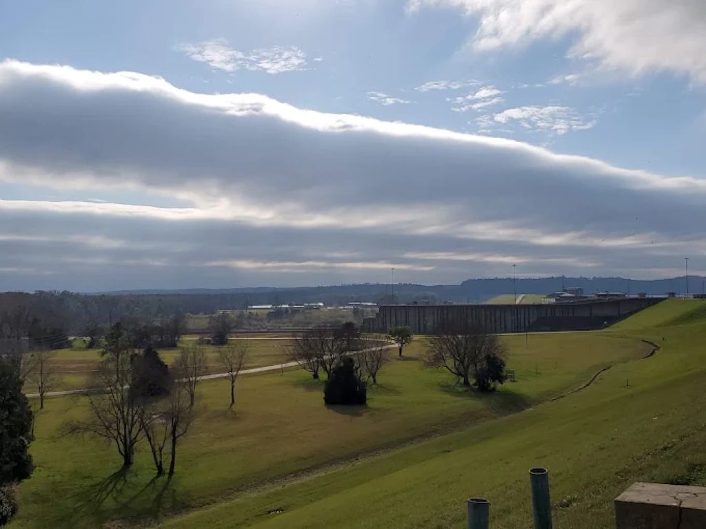 Paisatge amb un camp gran i obert, alguns arbres i un edifici a la distància.