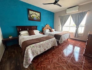 Une chambre d’hôtel avec deux lits, un ventilateur de plafond, un appareil de climatisation et une fenêtre avec des rideaux.