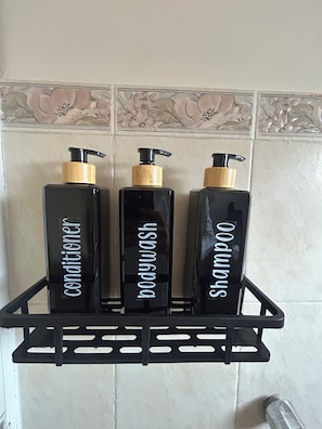 Trois bouteilles noires dotées de pompes doseuses, posées sur une étagère noire devant un mur carrelé.