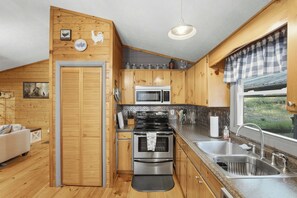 A compact kitchen with wooden cabinets, a stainless steel stove, a microwave, and a sink. - Bear Essentials & Hot Tub (Blairsville)