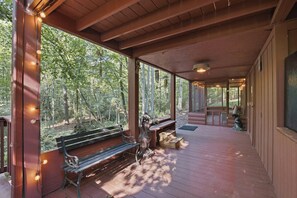 A covered outdoor area with a wooden bench, a statue, and a view of a forest. - Bear Essentials & Hot Tub (Blairsville)