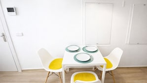 Un coin repas avec une table blanche, quatre chaises dotées de coussins jaunes et une porte blanche avec un interrupteur.